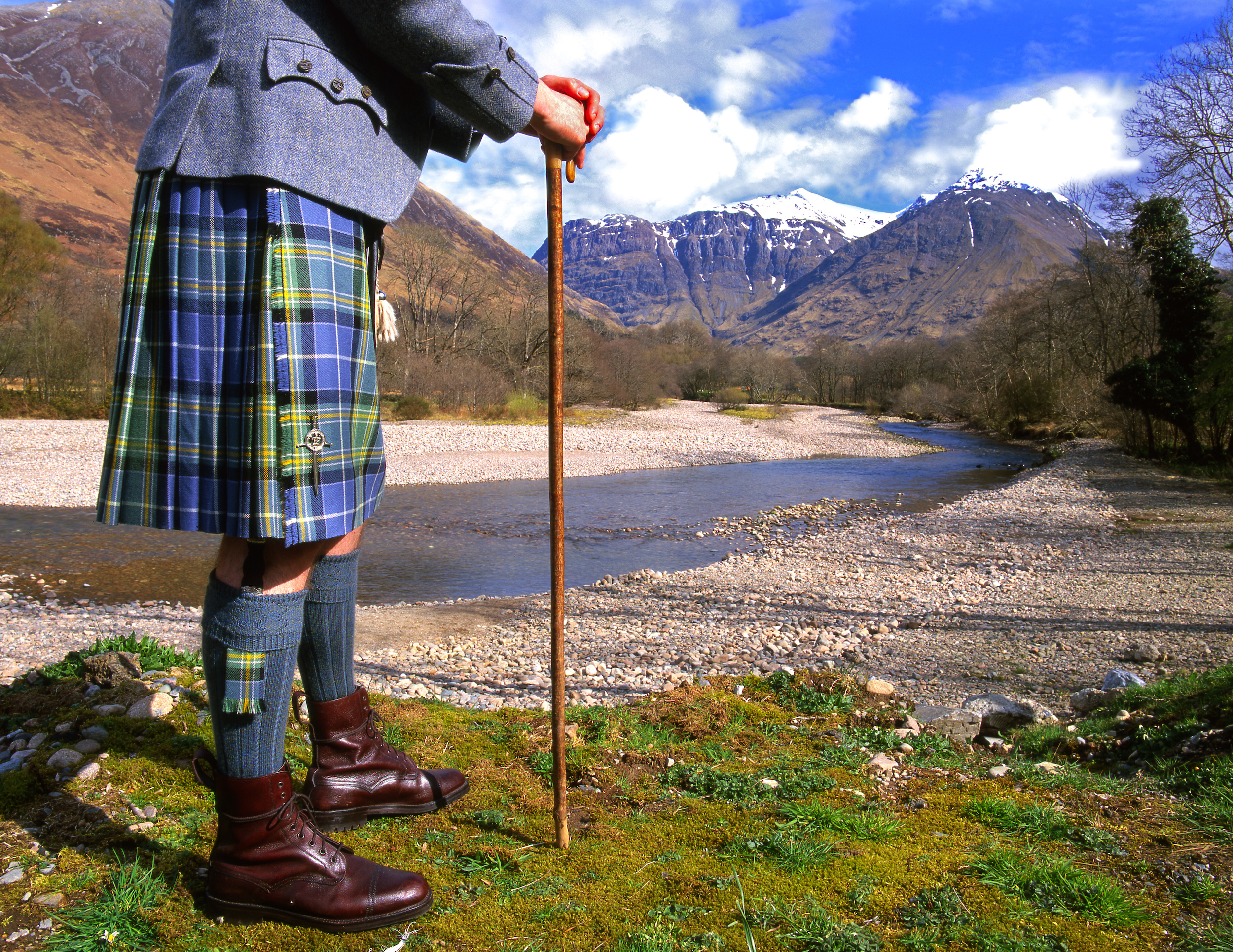 A kilted walker with a cromach beside the River Coe, the mountains of Glencoe behind